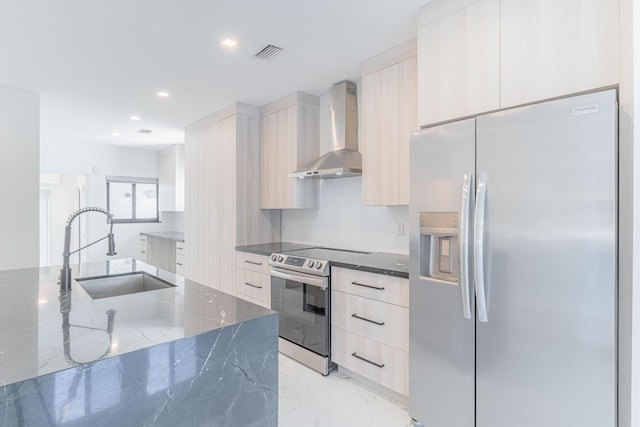 kitchen with light brown cabinetry, sink, dark stone countertops, appliances with stainless steel finishes, and wall chimney range hood