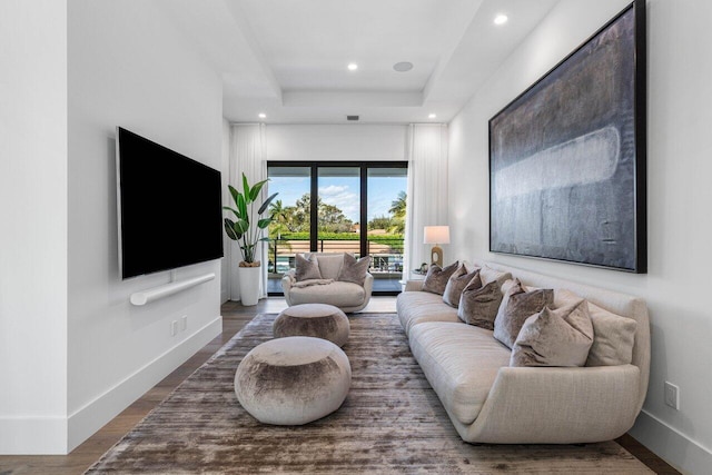 living area with a raised ceiling, recessed lighting, wood finished floors, and baseboards