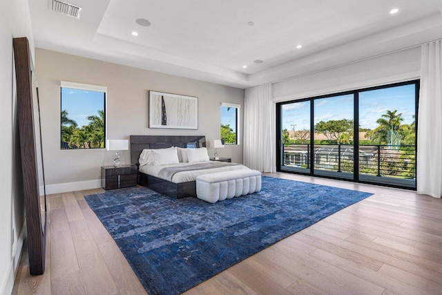 bedroom featuring access to exterior, wood-type flooring, visible vents, and a raised ceiling