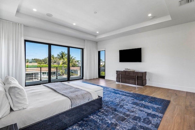 bedroom with a tray ceiling, wood finished floors, and access to exterior