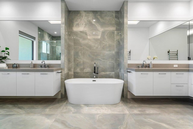 full bath featuring marble finish floor, a freestanding bath, two vanities, and a shower stall