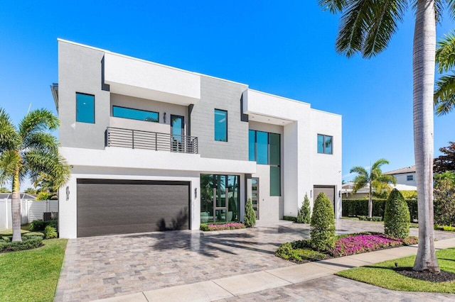 contemporary home featuring stucco siding, decorative driveway, a garage, and a balcony