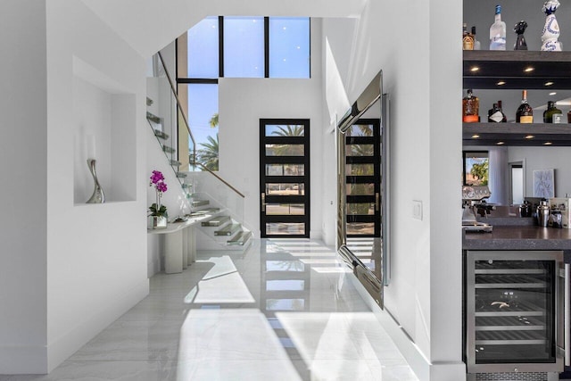 entrance foyer with wine cooler, marble finish floor, a dry bar, and a wealth of natural light