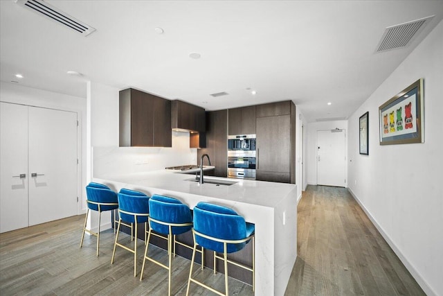 kitchen featuring dark brown cabinetry, a breakfast bar, sink, kitchen peninsula, and light hardwood / wood-style floors