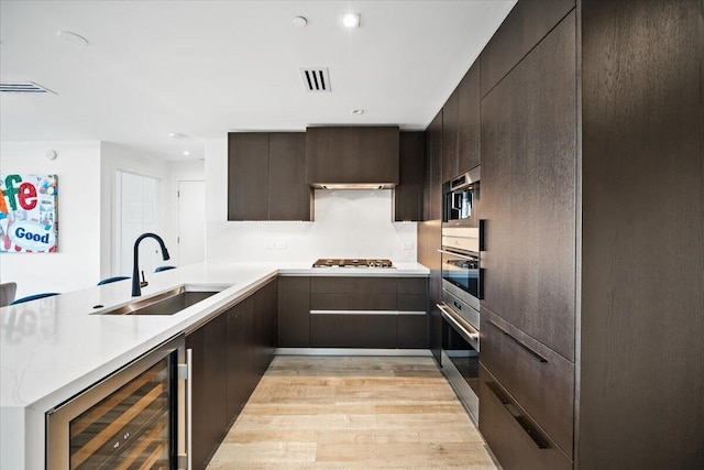 kitchen with sink, stainless steel oven, beverage cooler, and light hardwood / wood-style flooring