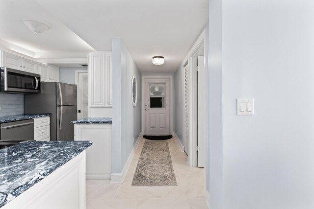 kitchen featuring sink, white cabinetry, stainless steel appliances, tasteful backsplash, and dark stone counters