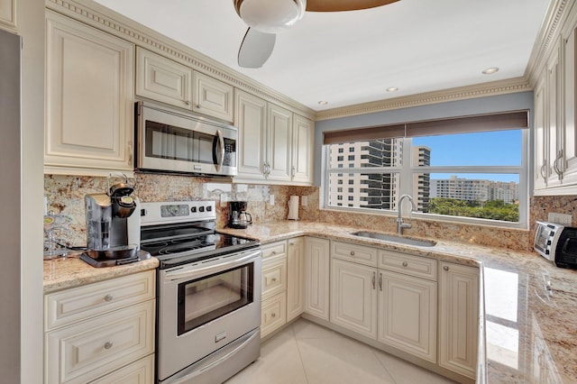 kitchen featuring sink, stainless steel appliances, light stone counters, decorative backsplash, and cream cabinetry