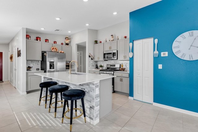 kitchen with appliances with stainless steel finishes, sink, gray cabinets, and an island with sink