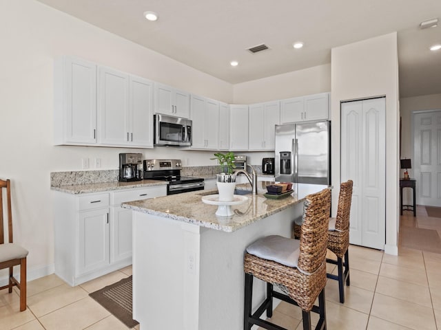 kitchen featuring a breakfast bar area, white cabinetry, stainless steel appliances, light stone counters, and a center island with sink