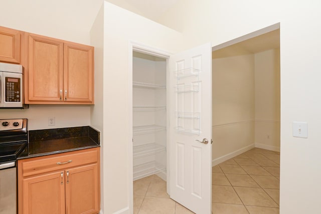 kitchen with dark stone countertops, stainless steel appliances, and light tile patterned floors