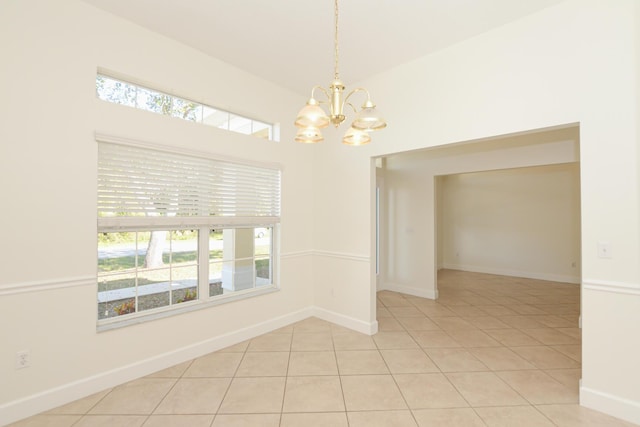 tiled spare room featuring a chandelier