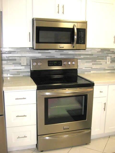 kitchen featuring stainless steel appliances, light tile patterned floors, white cabinets, and backsplash