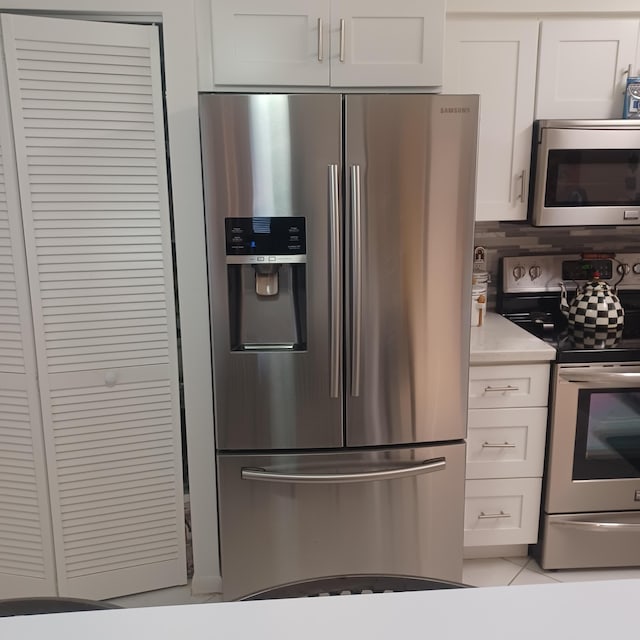 kitchen with light tile patterned floors, backsplash, white cabinets, and appliances with stainless steel finishes