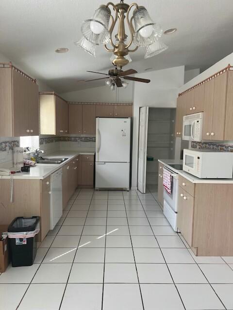 kitchen with light tile patterned flooring, vaulted ceiling, sink, backsplash, and white appliances