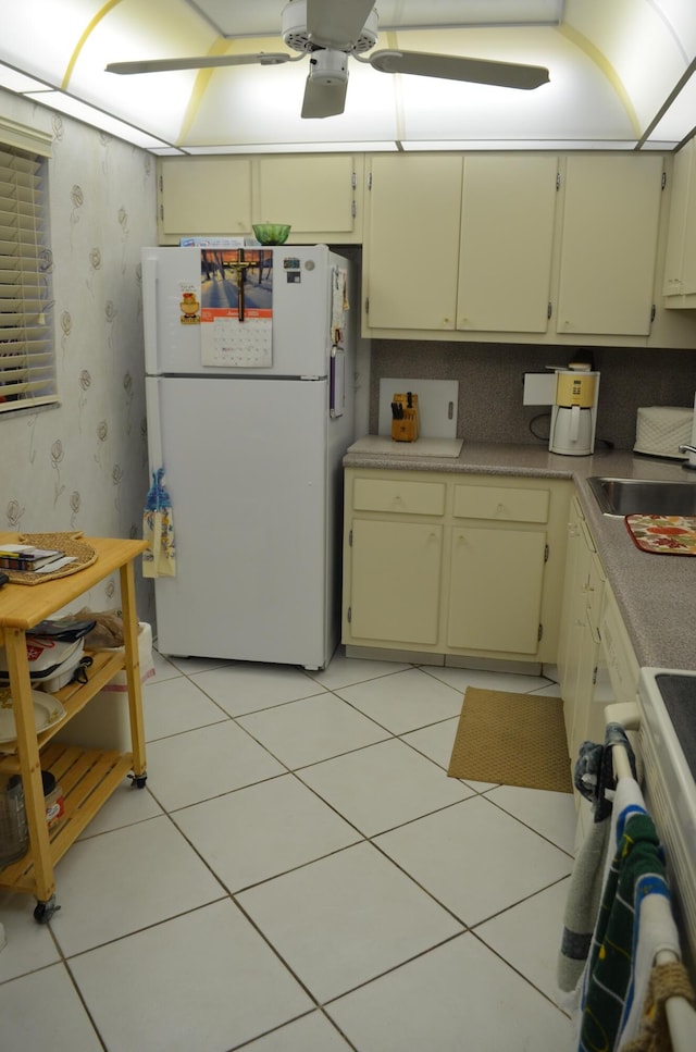 kitchen with sink, white fridge, range, light tile patterned floors, and cream cabinets