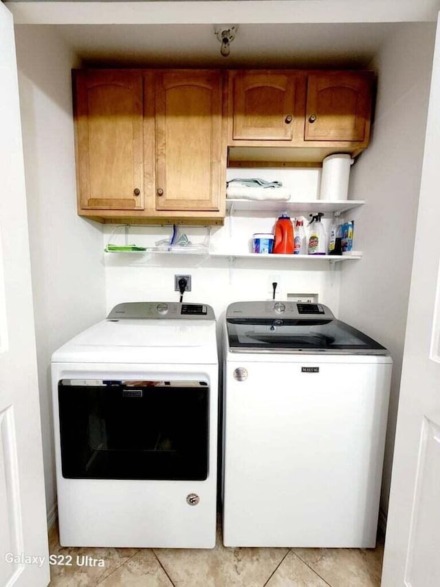 clothes washing area with light tile patterned flooring, cabinets, and washer and dryer