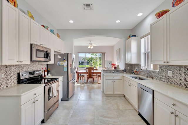 kitchen featuring appliances with stainless steel finishes, sink, backsplash, white cabinets, and ceiling fan