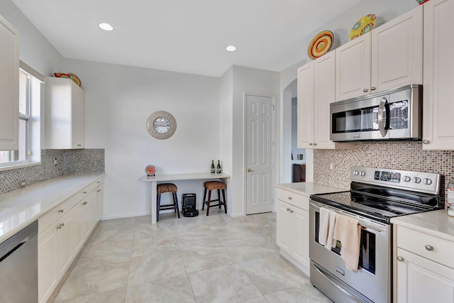 kitchen featuring white cabinetry, backsplash, light stone countertops, and appliances with stainless steel finishes