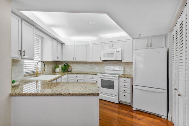 kitchen with a peninsula, white appliances, a sink, white cabinets, and dark wood finished floors