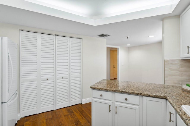 kitchen with light stone counters, freestanding refrigerator, white cabinets, and visible vents