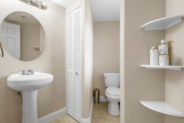 bathroom with tile patterned flooring, toilet, a sink, baseboards, and a closet