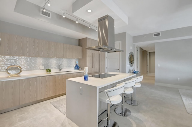 kitchen with sink, a breakfast bar, island range hood, a kitchen island, and black electric cooktop