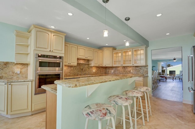 kitchen featuring a kitchen island, tasteful backsplash, a breakfast bar area, light stone counters, and stainless steel double oven