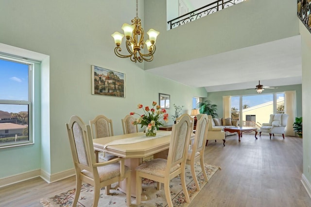 dining room with a high ceiling, ceiling fan with notable chandelier, and light wood-type flooring