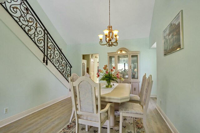 dining space featuring ceiling fan with notable chandelier, light wood finished floors, a towering ceiling, and baseboards