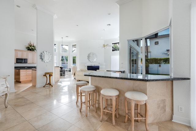 kitchen with a towering ceiling, light brown cabinetry, ceiling fan, and kitchen peninsula