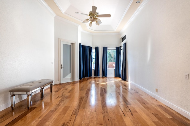 empty room featuring crown molding, a tray ceiling, light hardwood / wood-style floors, and ceiling fan