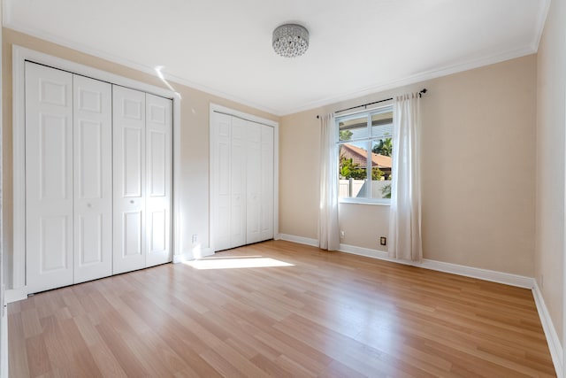 unfurnished bedroom featuring crown molding, two closets, and light wood-type flooring