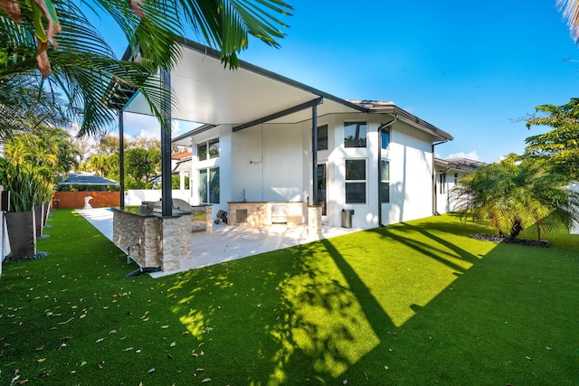 back of house featuring a bar, a patio area, a lawn, and exterior kitchen