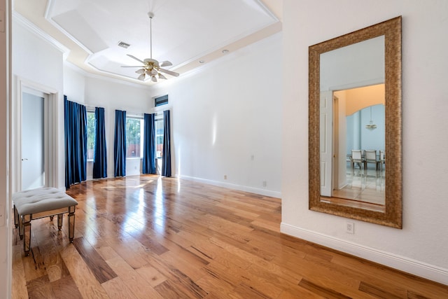 unfurnished room featuring a towering ceiling, ceiling fan, a tray ceiling, crown molding, and light wood-type flooring