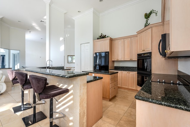 kitchen featuring dark stone countertops, kitchen peninsula, light brown cabinetry, and black appliances