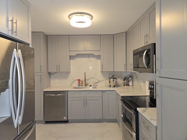 kitchen featuring sink, appliances with stainless steel finishes, gray cabinetry, backsplash, and light stone counters