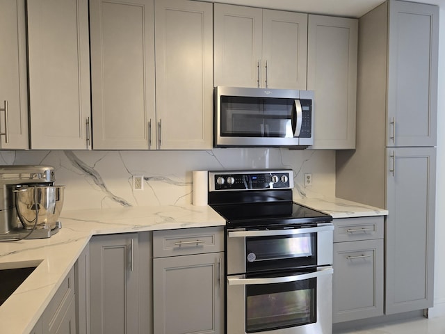 kitchen with stainless steel appliances, gray cabinets, light stone countertops, and backsplash