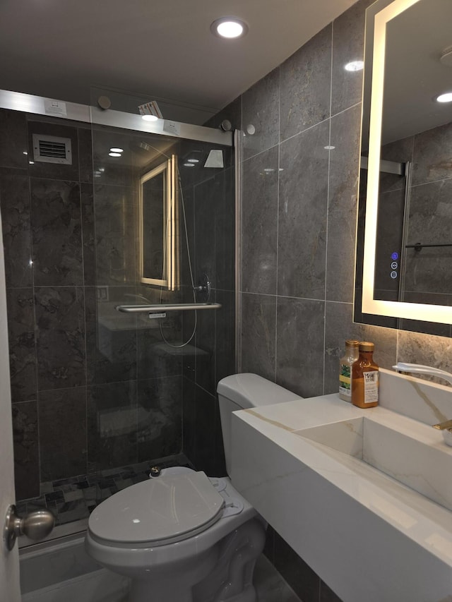 bathroom featuring vanity, toilet, a shower with shower door, and tile walls