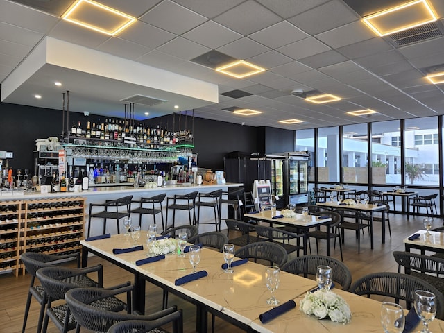 dining room featuring expansive windows, indoor bar, hardwood / wood-style floors, and a drop ceiling