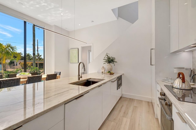 kitchen with sink, light hardwood / wood-style flooring, white cabinetry, light stone counters, and built in microwave