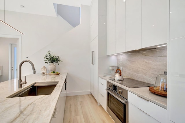 kitchen with sink, white cabinetry, light stone countertops, black electric cooktop, and oven