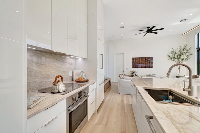 kitchen with sink, white cabinetry, light stone counters, black electric cooktop, and oven