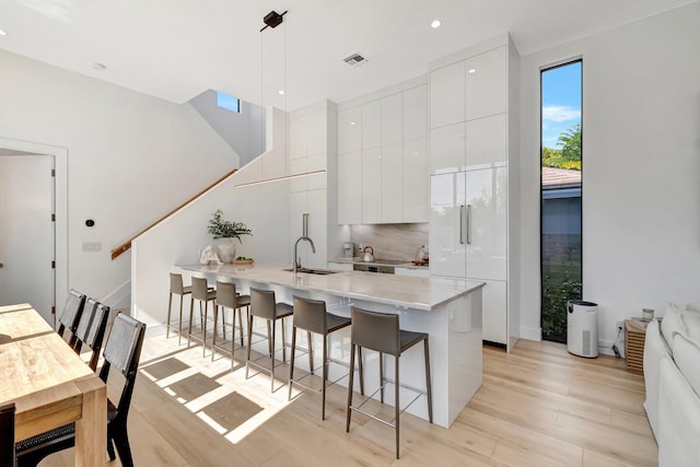 kitchen featuring a kitchen island with sink, hanging light fixtures, a breakfast bar, and white cabinets