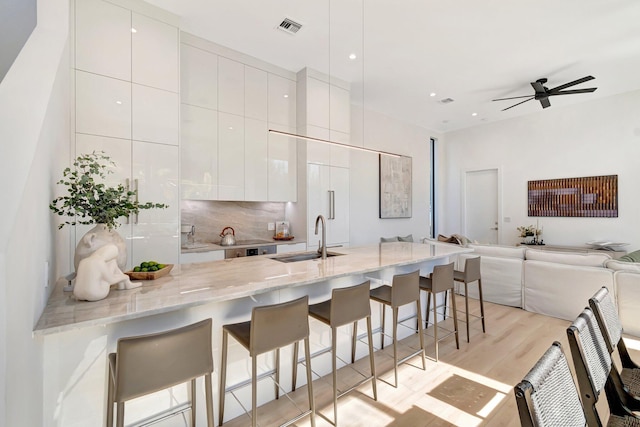 kitchen with light stone counters, sink, a breakfast bar, and white cabinets