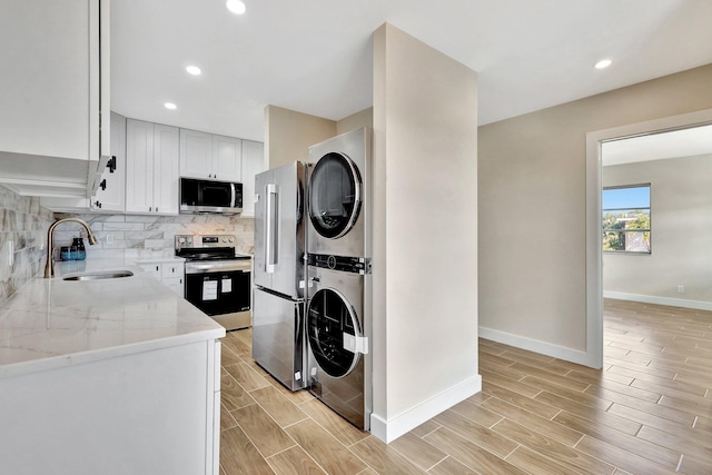 kitchen featuring appliances with stainless steel finishes, sink, white cabinets, backsplash, and stacked washer and clothes dryer