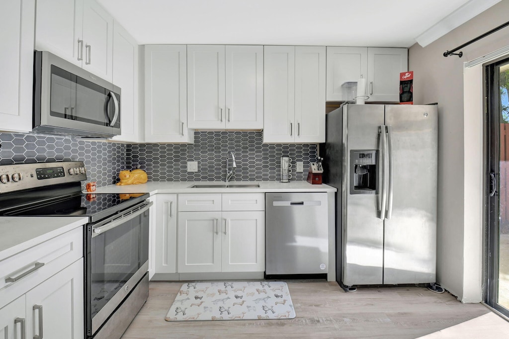 kitchen with white cabinetry, stainless steel appliances, sink, and decorative backsplash