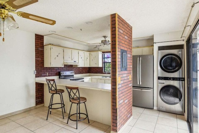 kitchen featuring ceiling fan, appliances with stainless steel finishes, a kitchen breakfast bar, stacked washer and clothes dryer, and kitchen peninsula