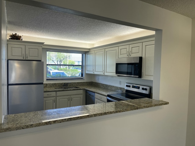 kitchen with appliances with stainless steel finishes, sink, white cabinets, dark stone counters, and a textured ceiling