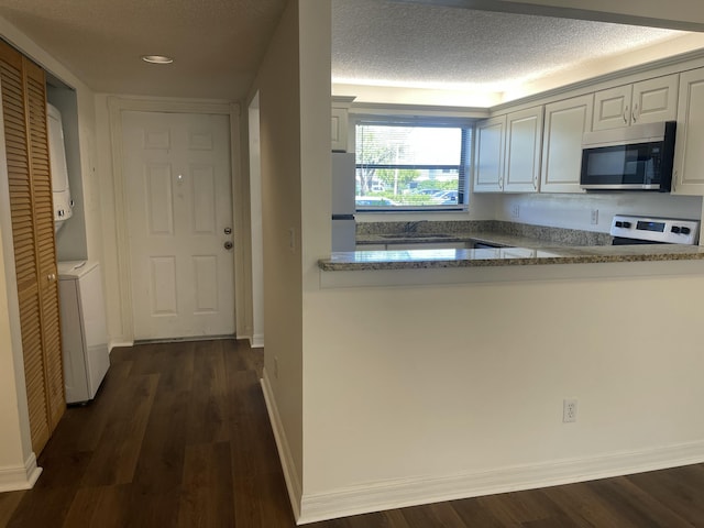 kitchen featuring stacked washer / drying machine, a textured ceiling, dark hardwood / wood-style flooring, stainless steel appliances, and light stone countertops