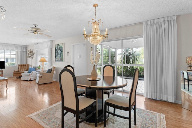 dining space with ceiling fan with notable chandelier, light hardwood / wood-style flooring, and a textured ceiling